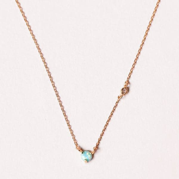 A dainty gold chain necklace with a circular opal stone in the center.