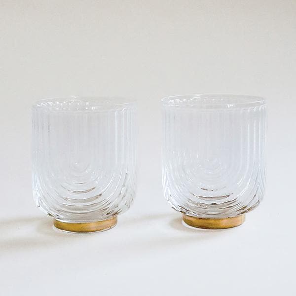 A clear glass tumbler with a gold base and an etched upside down arched design.