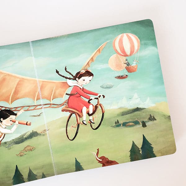 On an ivory background is the book open to a page in the book showing a girl flying through the air on a bicycle. 