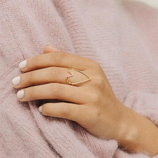 On a model&#39;s finger is a thin heart shaped ring with the center left open.