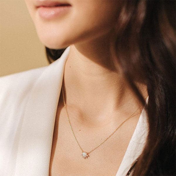 A dainty gold necklace with a round opal pendant in the center that is lined with cz stones around the bottom edge.