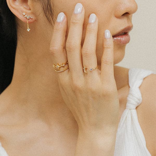 A gold ring with an open front that features a cubic zirconia on one end and a crescent moon on the other, photographed worn on a models hand.