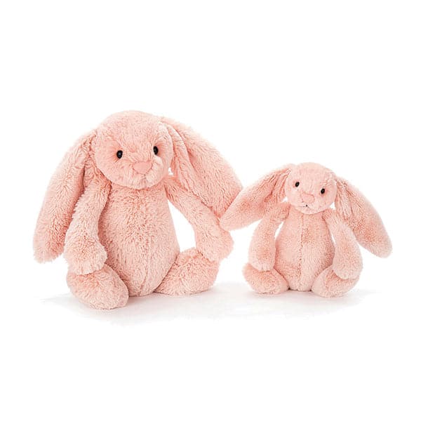 Two, one large and small, soft stuffed animals in the shape of pink blush colored rabbits with long floppy ears, arms and legs.