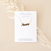"Katie Dear Jewelry" white card with gold necklace in the shape of the word "Auntie"