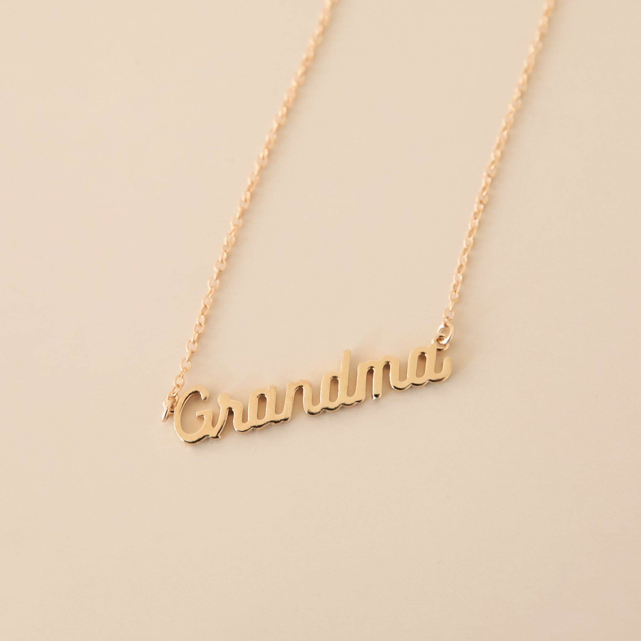 A dainty gold chain necklace with gold letters that read, "Grandma" as a pendant.
