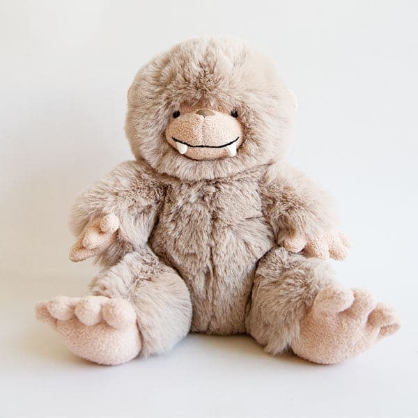 A tan fuzzy Bigfoot stuffed animal with a round head, white teeth and big hands and feet.