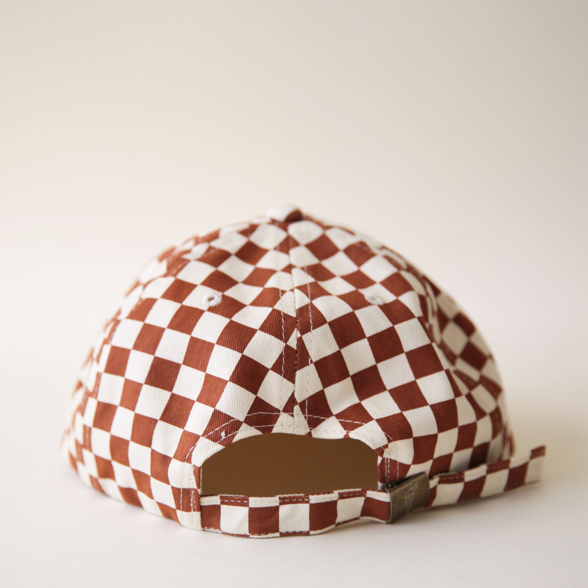 A white and rust checkered six panel hat and features a fabric strap with brass metal clasp.  Edit alt text