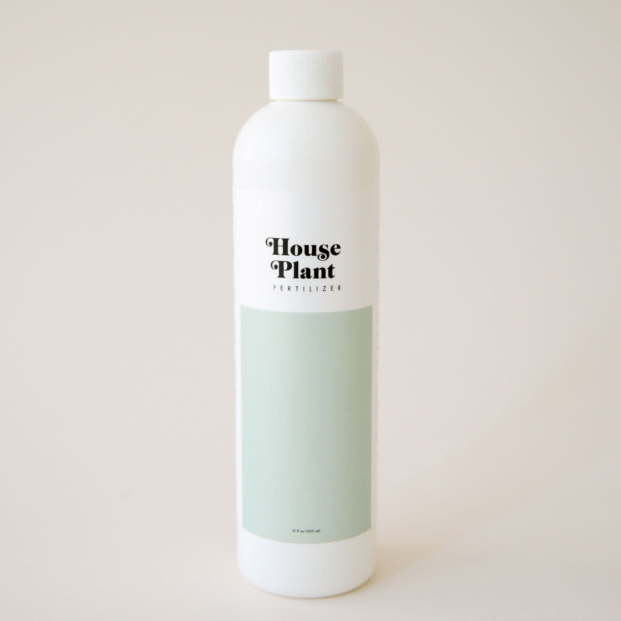 On a cream background is a white plastic bottle of fertilizer with a light teal rectangular shape on the bottom half and text on the top that reads, "House Plant Fertilizer" in black letters. 