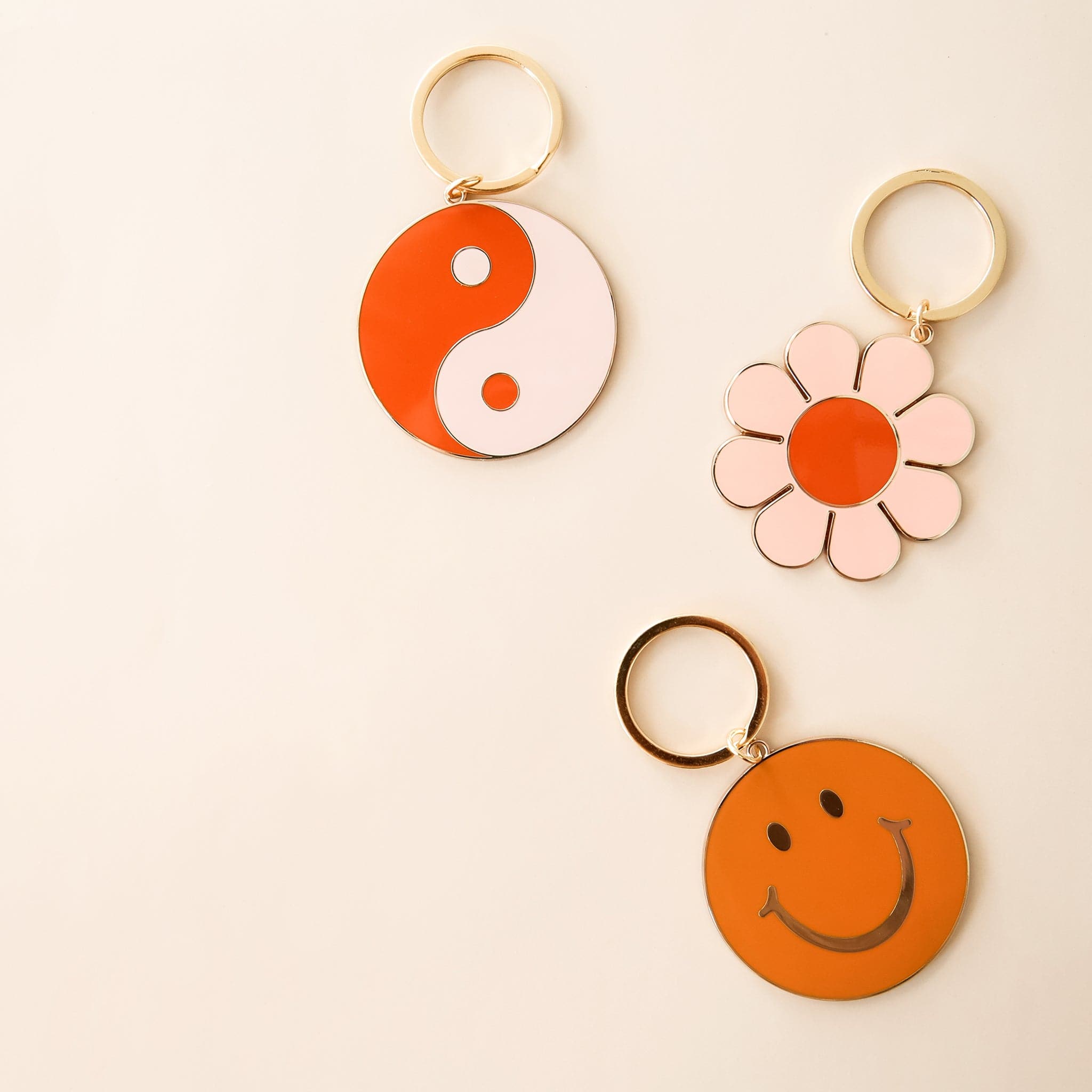 Three keychains including a yin-yang symbol, flower, and smiley face. Each keychain has gold detailing and a golden key ring.