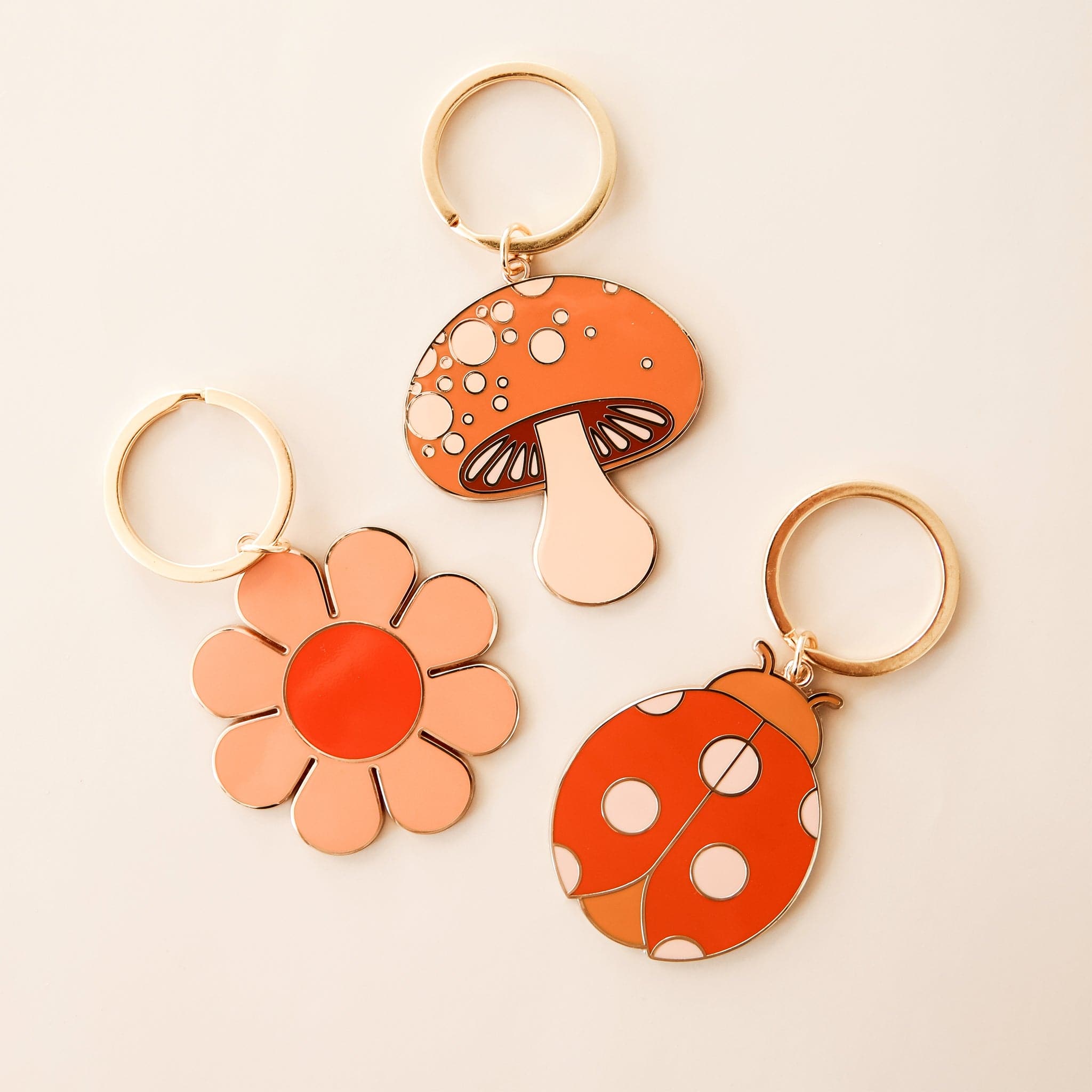 Three retro-inspired keychains, including a flower, mushroom and lady bug. Each keychain has gold detailing and a golden key ring. 