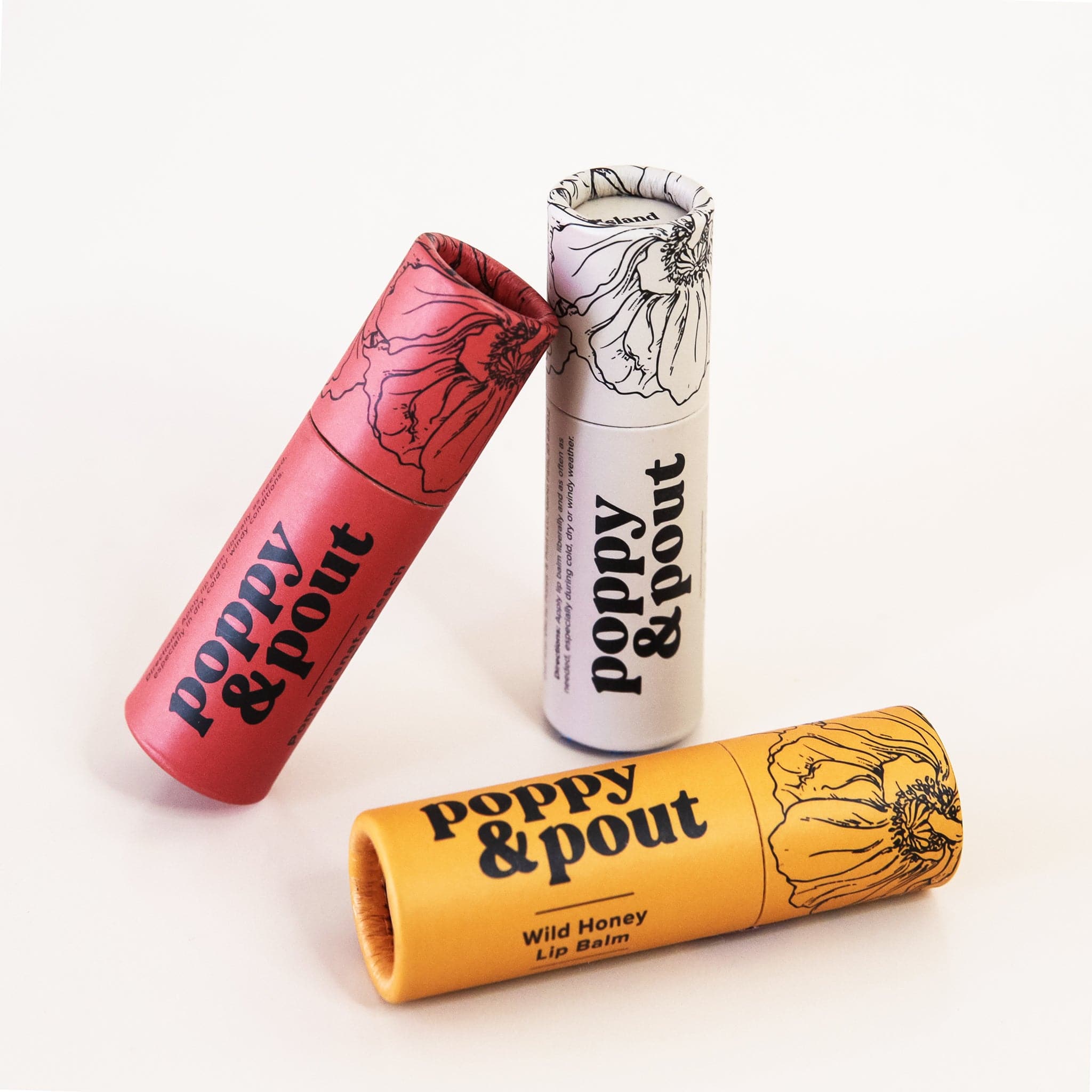 In front of a white background is a yellow tube. On the right side is a black drawing of a flower. On the left is black text that reads ‘poppy & pout.’ Standing up behind this tube is a dark red and white tube. 