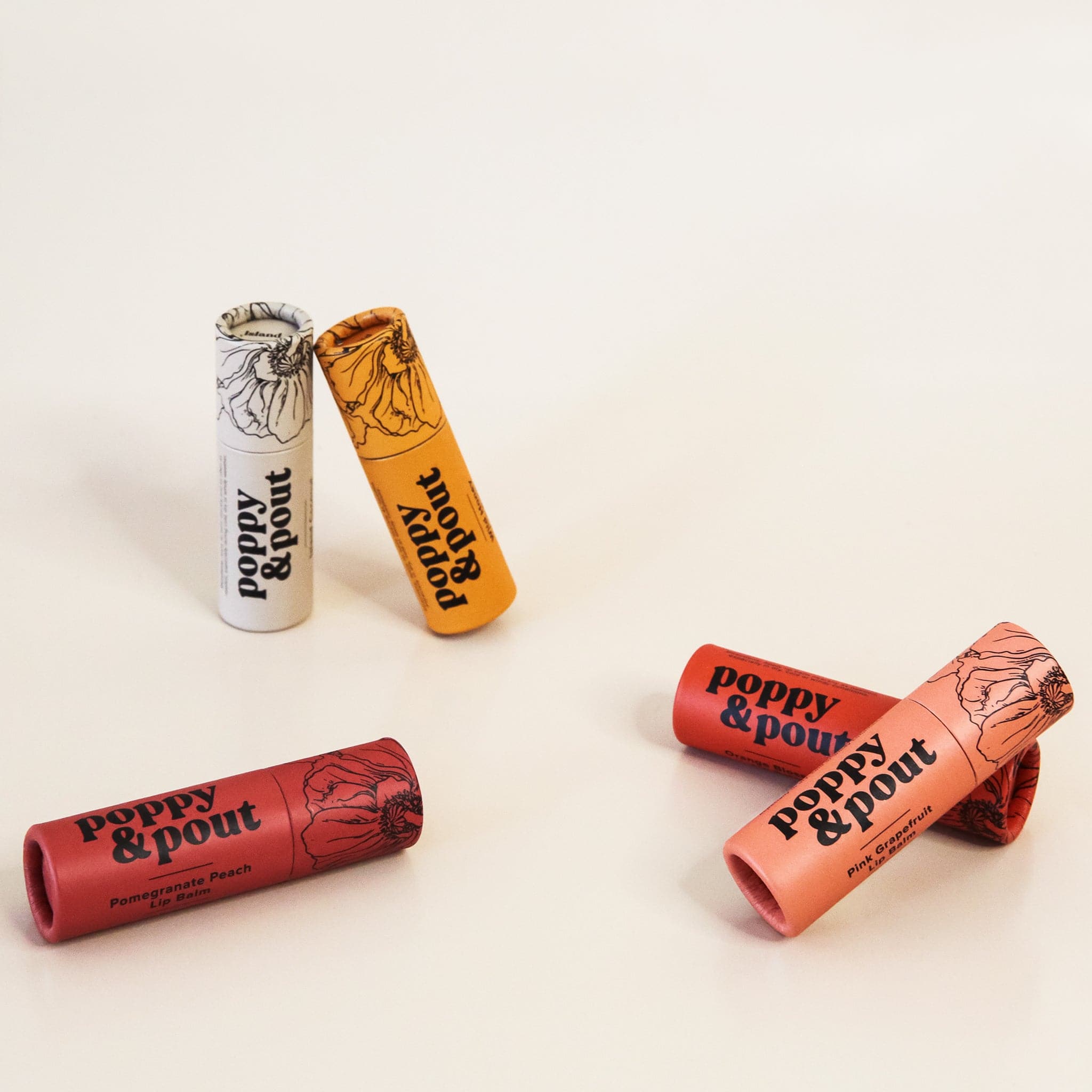 In front of a white background is five round tubes. Each tube has black text that reads ‘poppy & pout.’ On the top is the black outline of a flower. Starting on the far left the colors are bright red, peach, gray, light orange and maroon. 