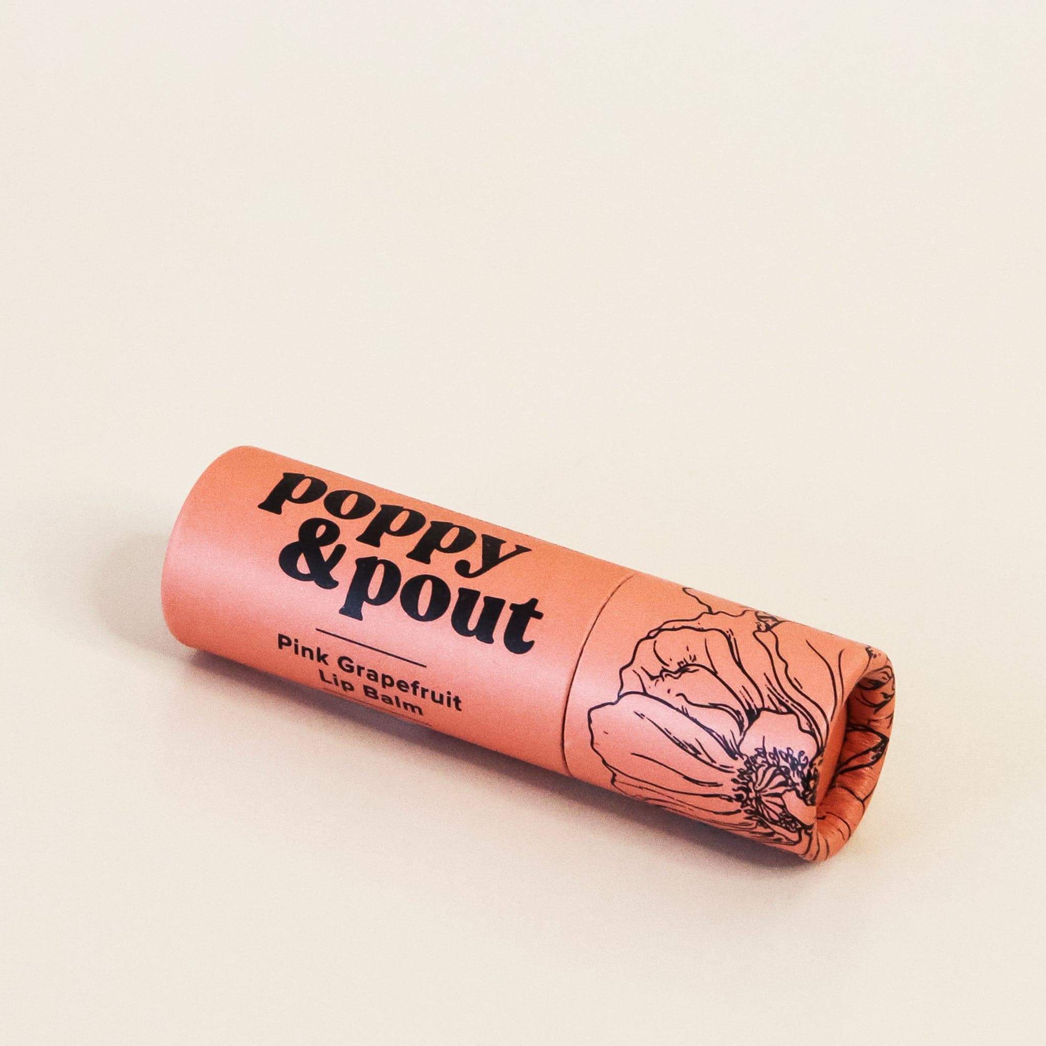 In front of white background is a round peach tube. On the right side is a black drawing of a flower. On the right side is black text that reads ‘poppy &amp; pout, pink grapefruit lip balm.&#39;
