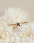On a cream background is a dainty gold ring with an "A" in the center.