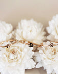 On a cream background is three dainty gold rings with a different initial in the center of each ring. 