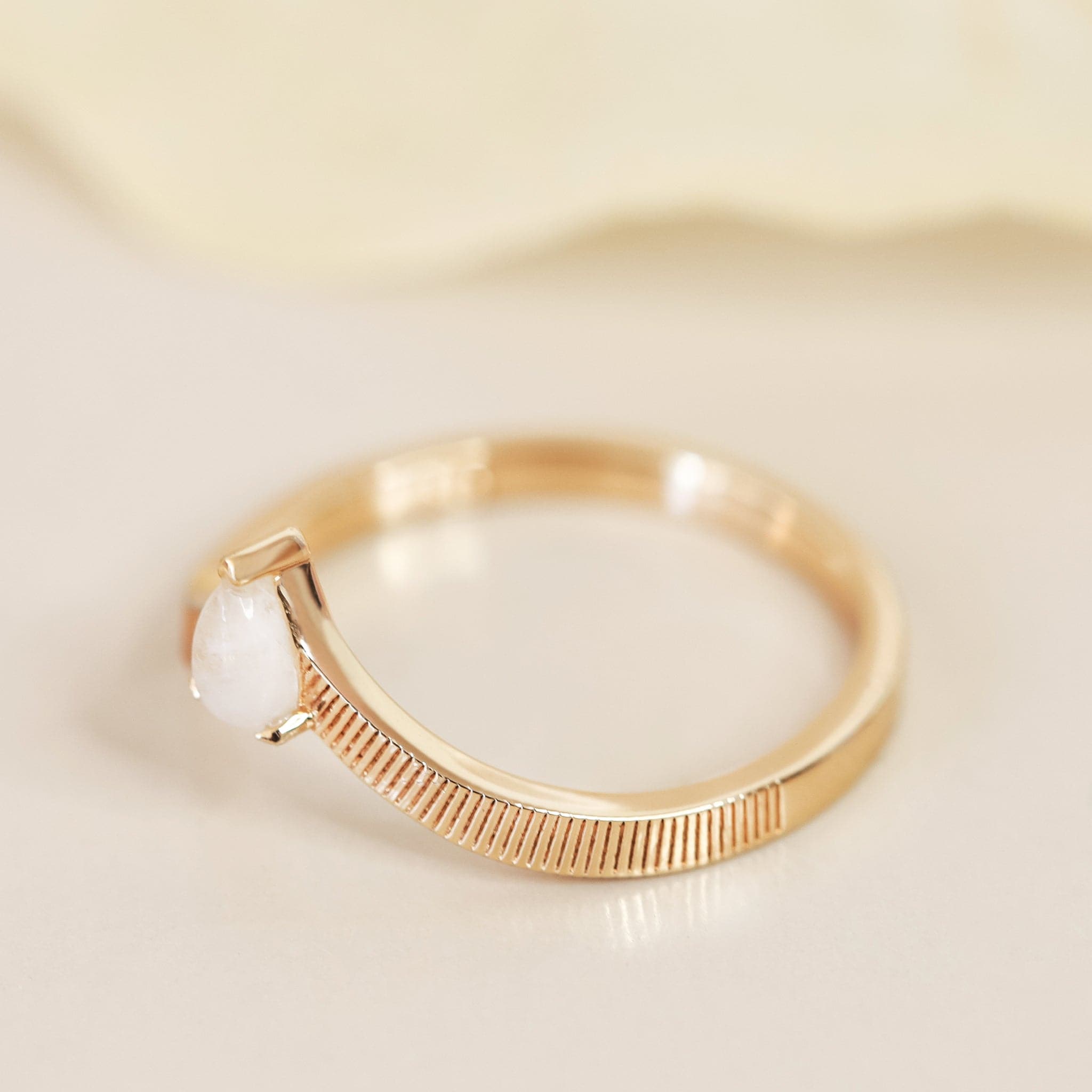 A gold band ring with etched line detailing and a white moonstone in the center.
