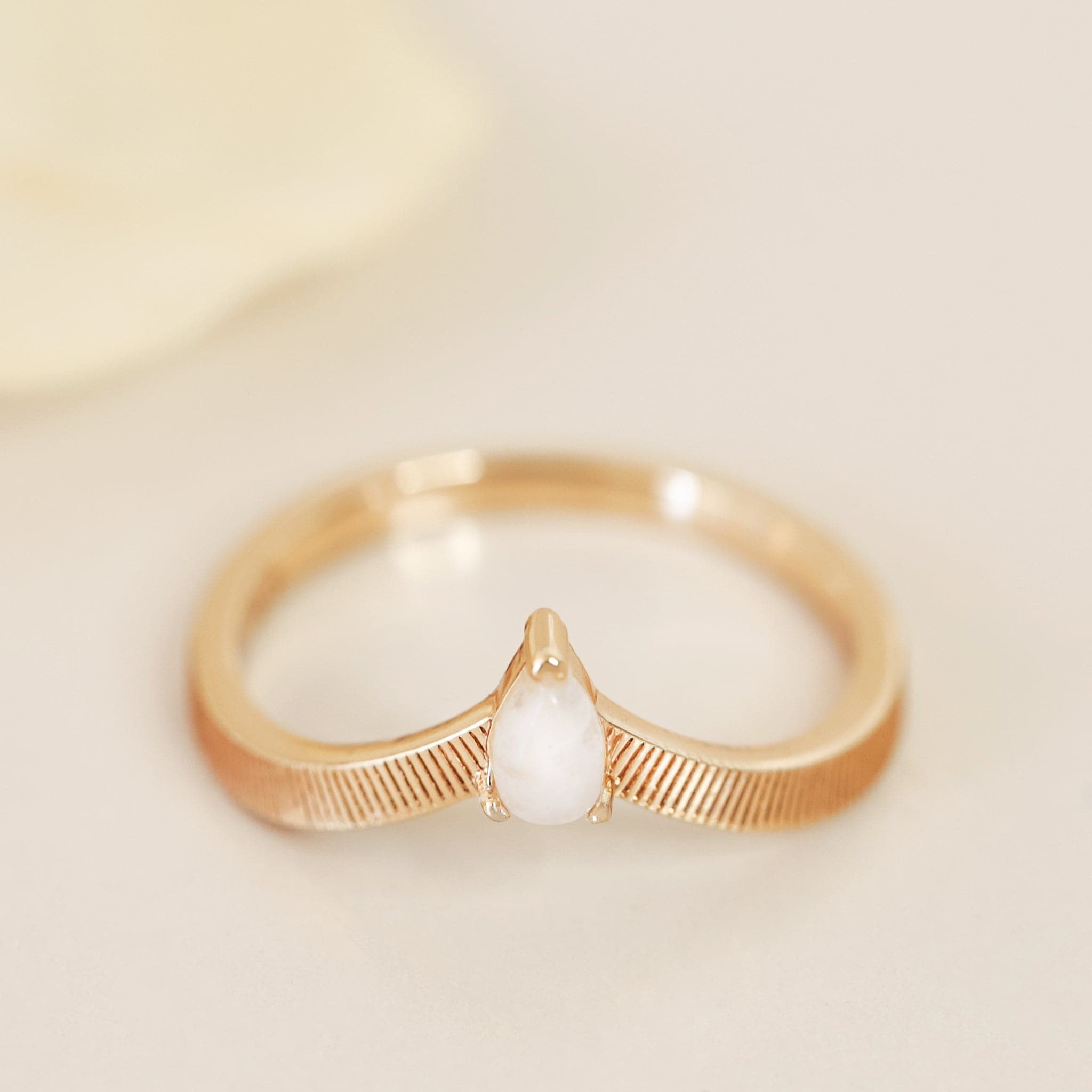 A gold band ring with etched line detailing and a white moonstone in the center.