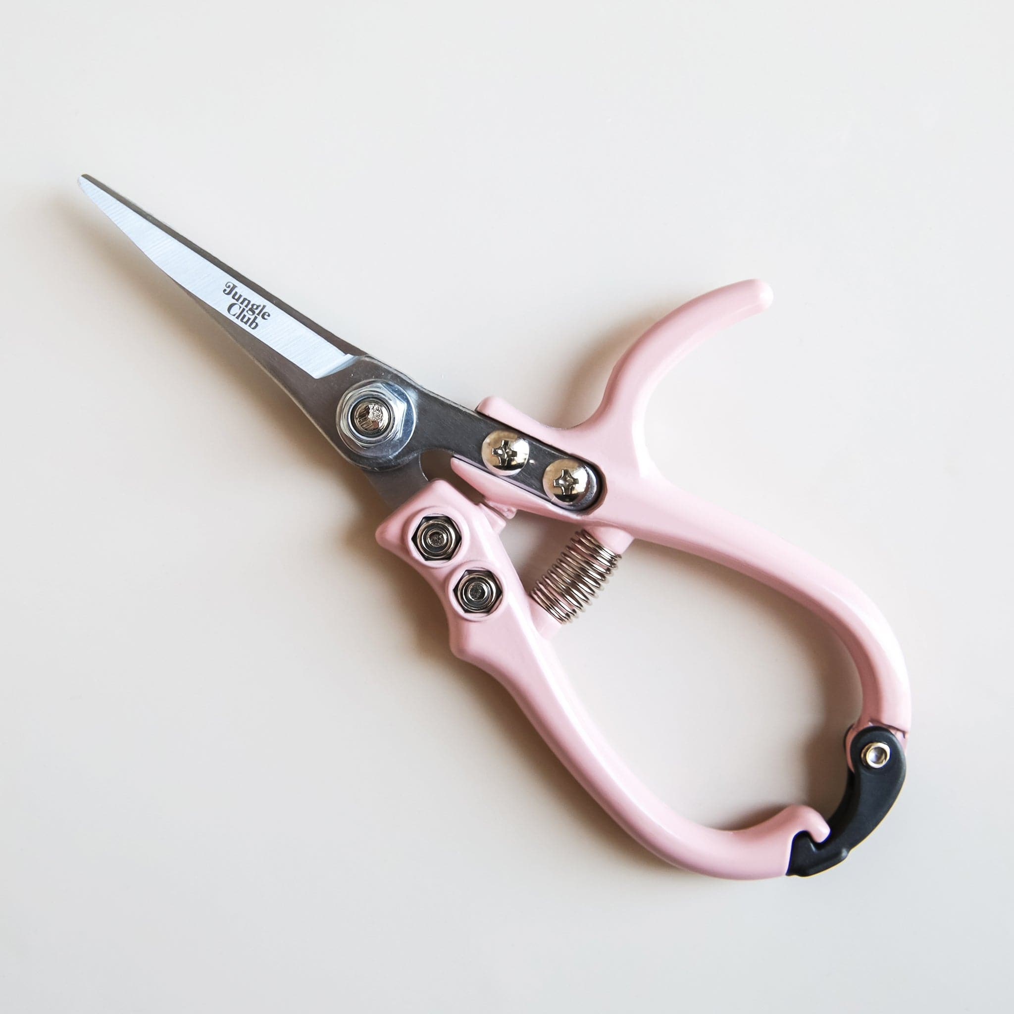 Pair of pruning shears with pastel pink handles and metal blades. The outer blade reads &#39;jungle club&#39; in small, playful lettering. The pruning shears have a black clasp at the top of the handles to secure them closed. 