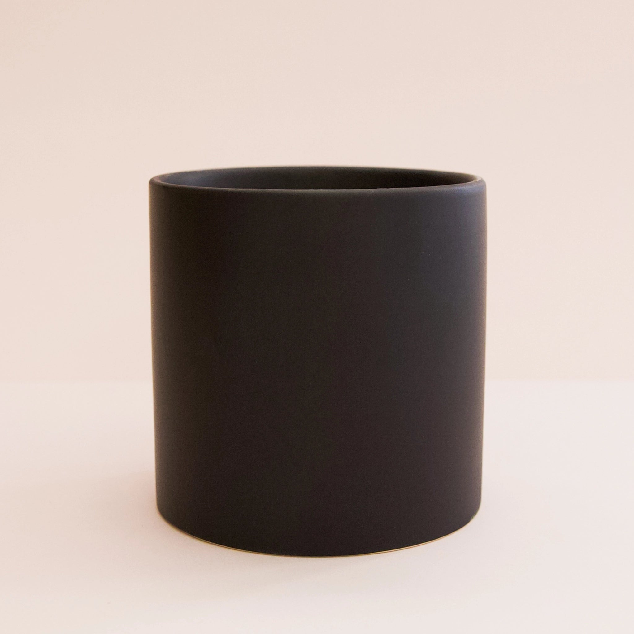On a white background is a matte black circle ceramic planter.