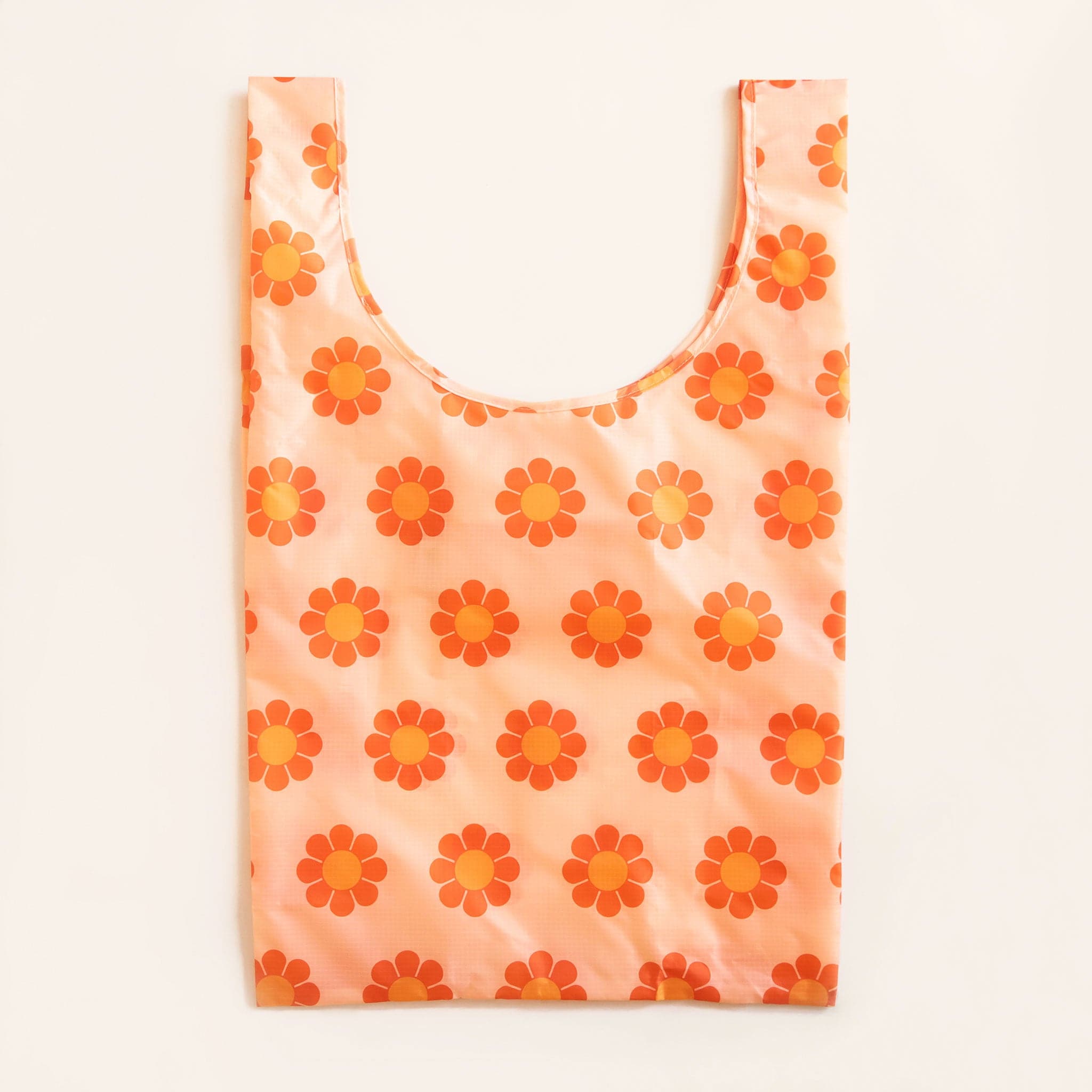 Peach reusable bag filled with a pattern of flowers with red-orange petals and tangerine centers. The bag is positioned flat on a table and has a &#39;U&#39; shape between two handles.