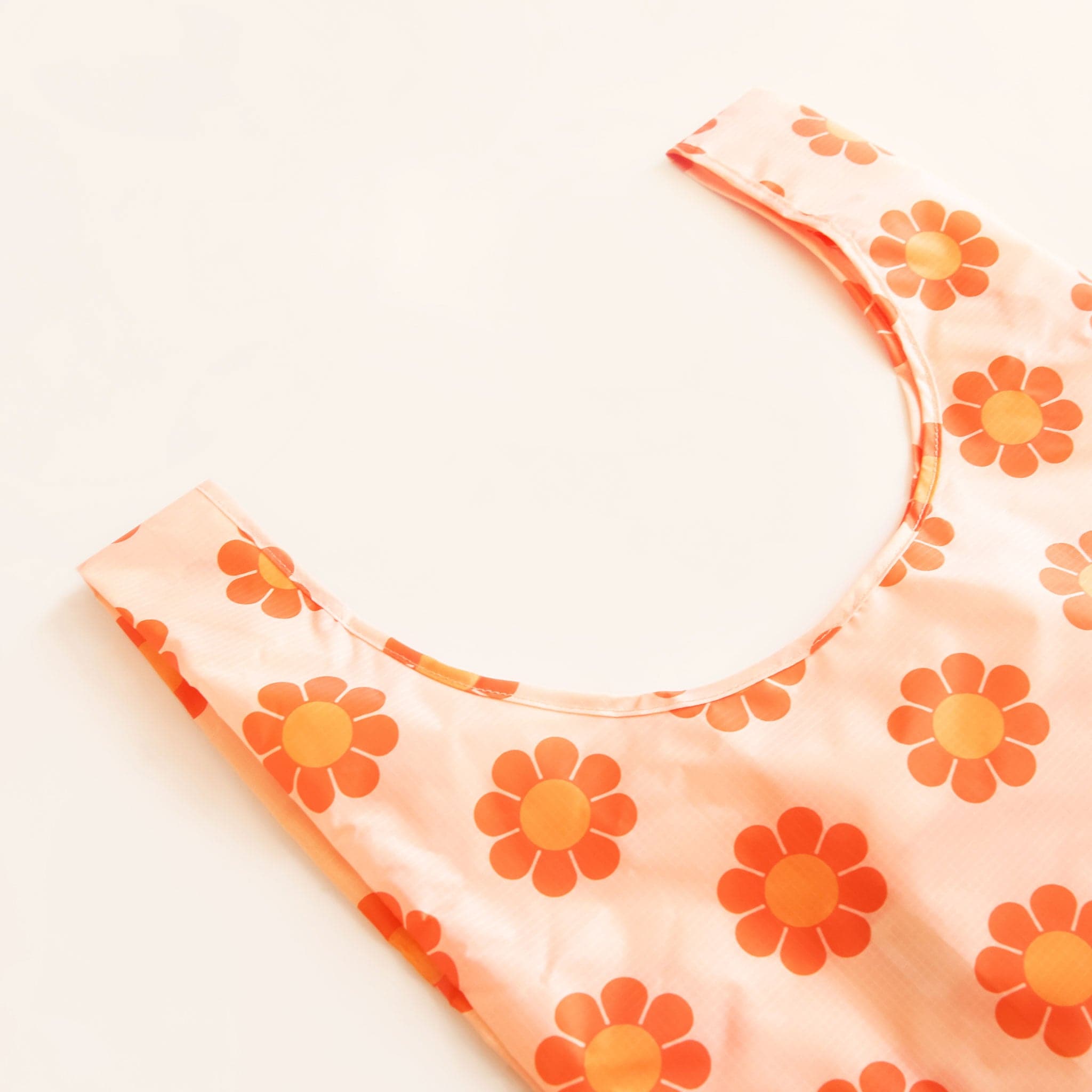 Peach reusable bag filled with a pattern of flowers with red-orange petals and tangerine centers. The bag is positioned flat on a table and has a &#39;U&#39; shape between two handles. 