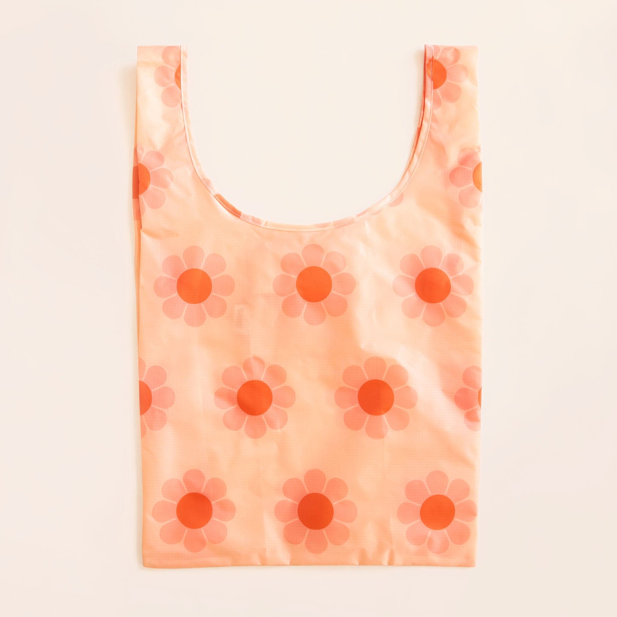 Peach reusable bag filled with a pattern of flowers with pink petals and red-orange centers. The bag is positioned flat on a table and has a &#39;U&#39; shape between two handles.