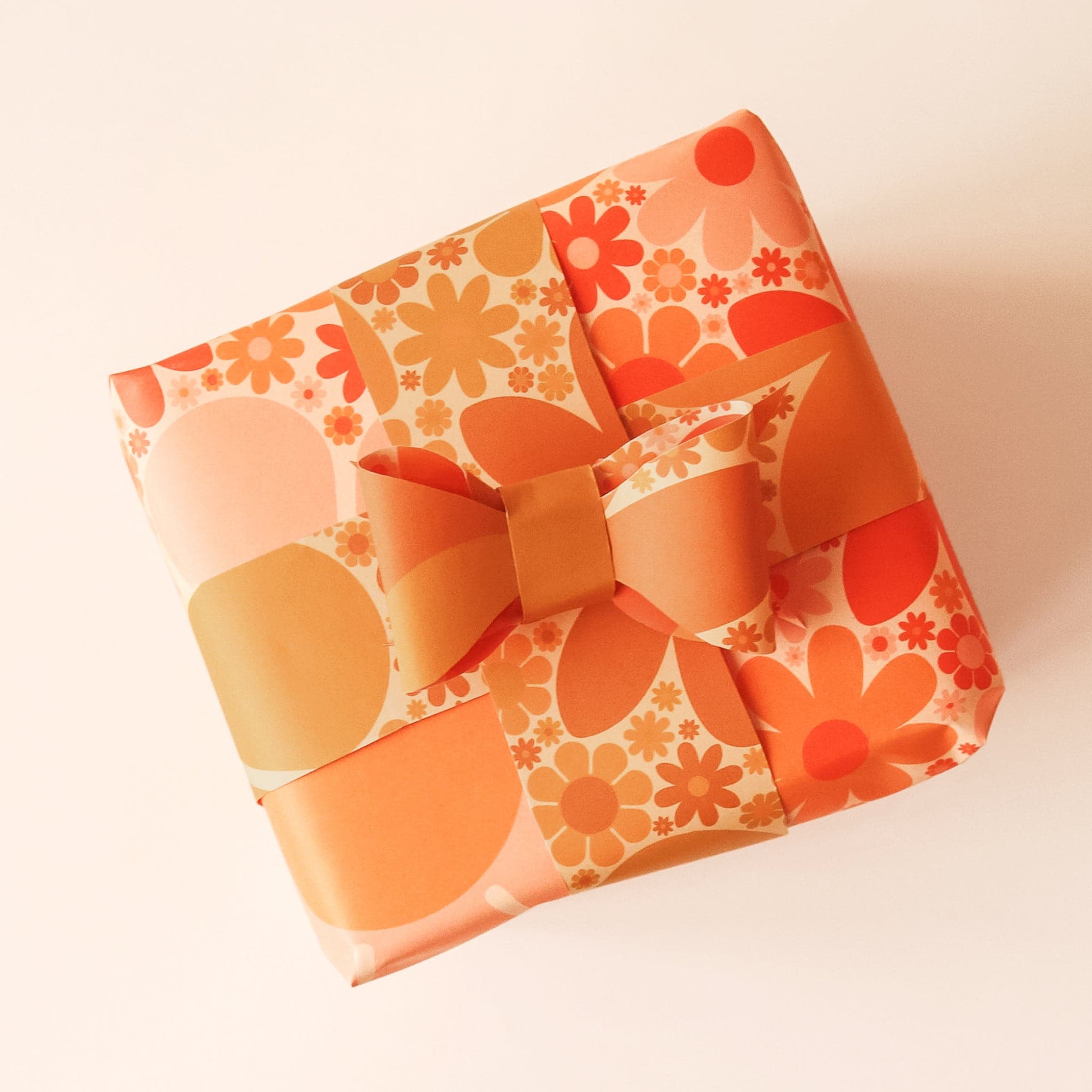 Wrapped present covered in retro-inspired yellow and orange floral wrapping paper. Thin strips of wrapping paper with smaller similar print stretch around the present and fasten into a bow.