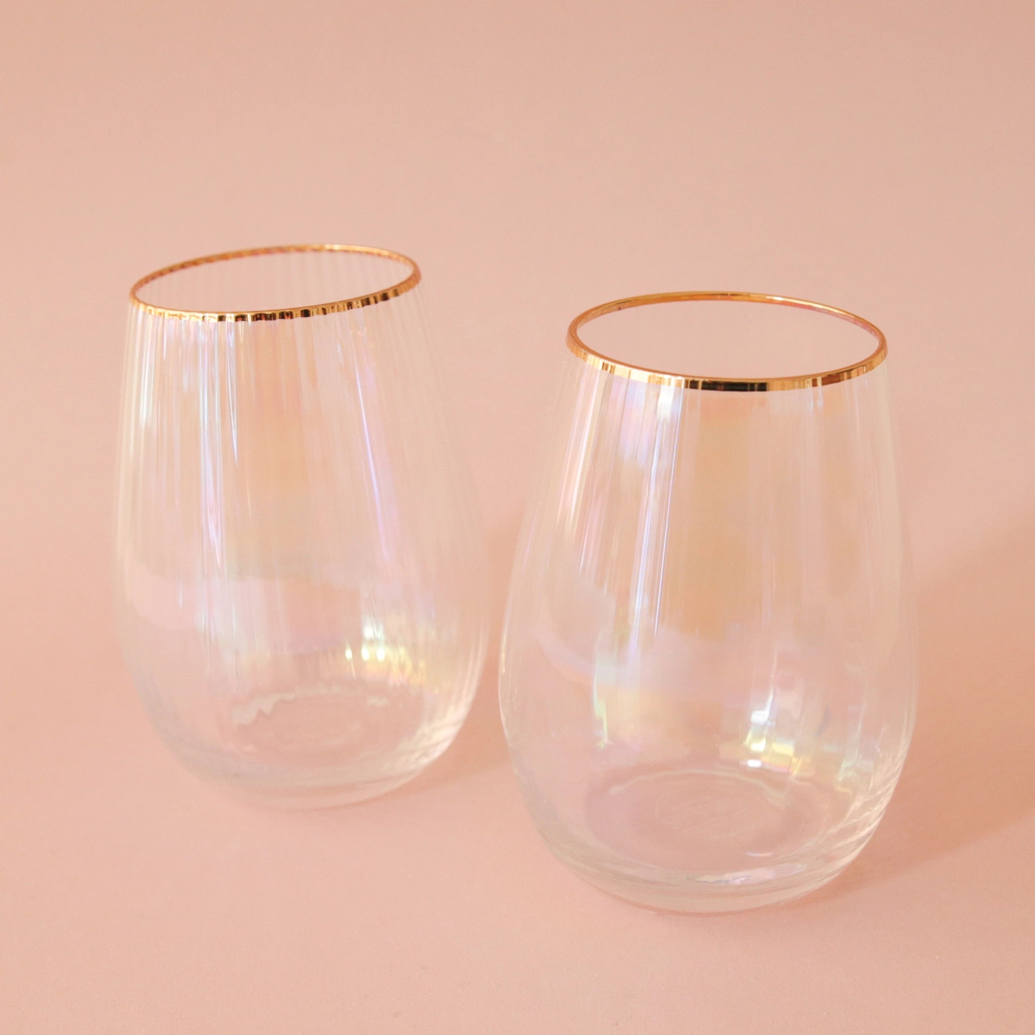 A stemless beveled wine glasses with an iridescent color and a gold rim.