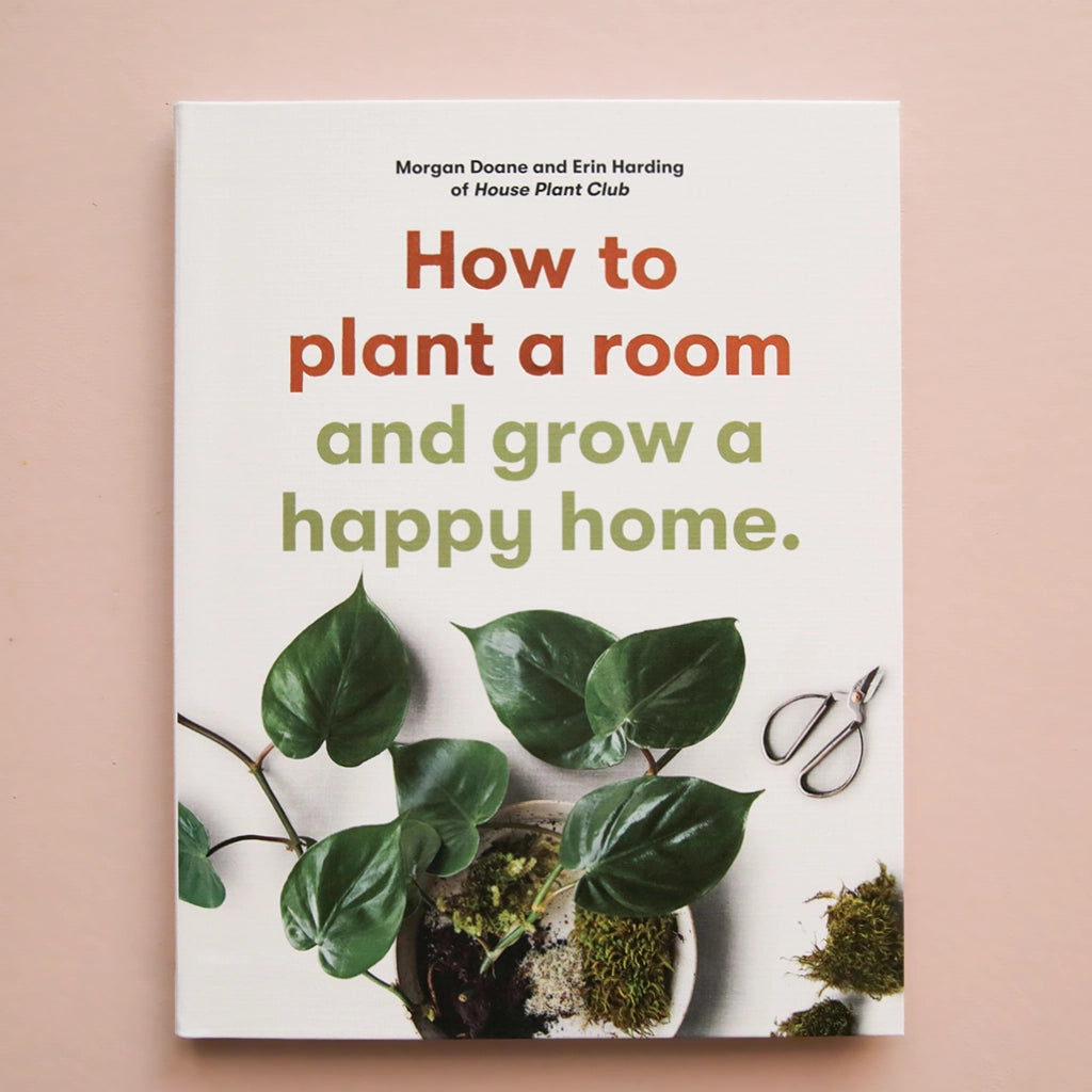 A white book with a green leafy plant and a title that reads, "How to plant a room and grow a happy home."
