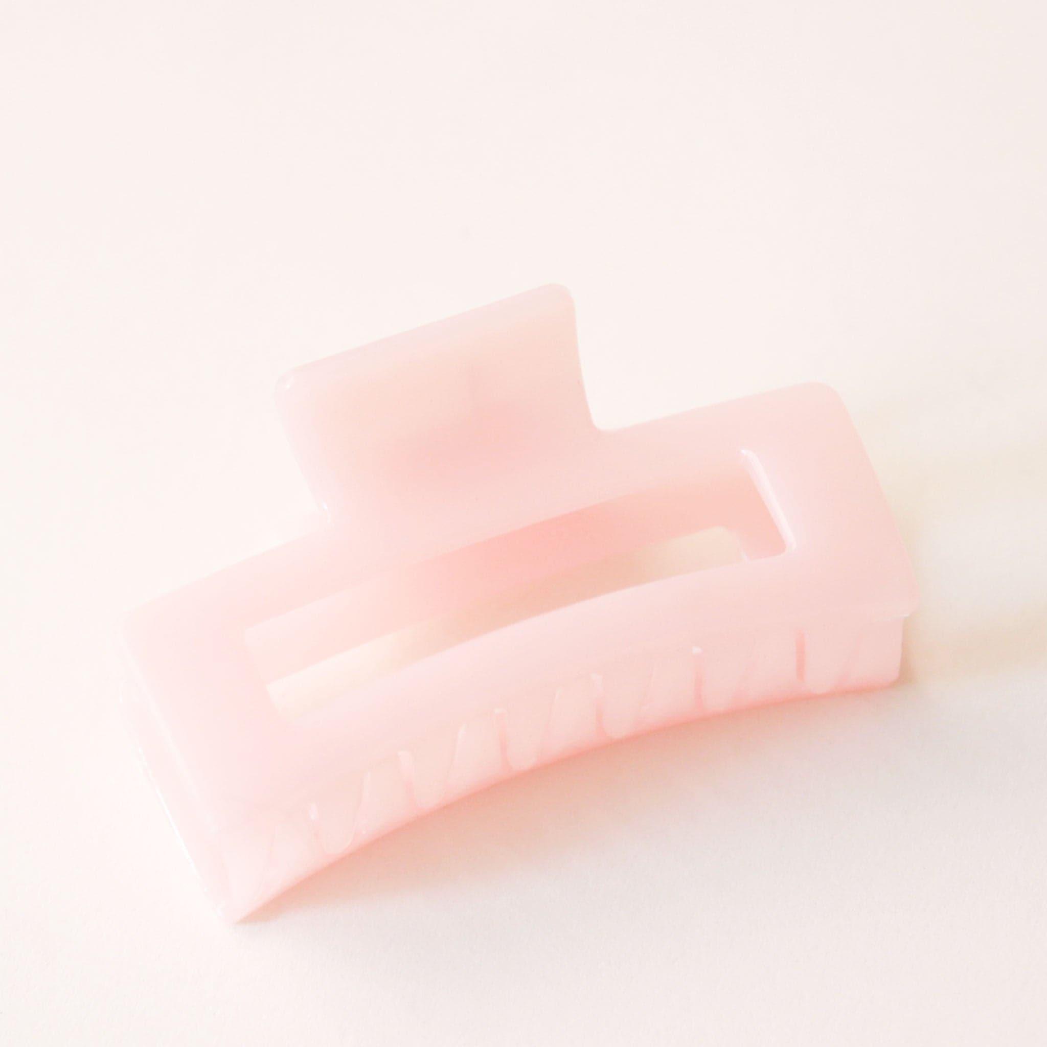 On a white background is a light pink colored rectangular claw clip with a jelly, almost translucent effect.