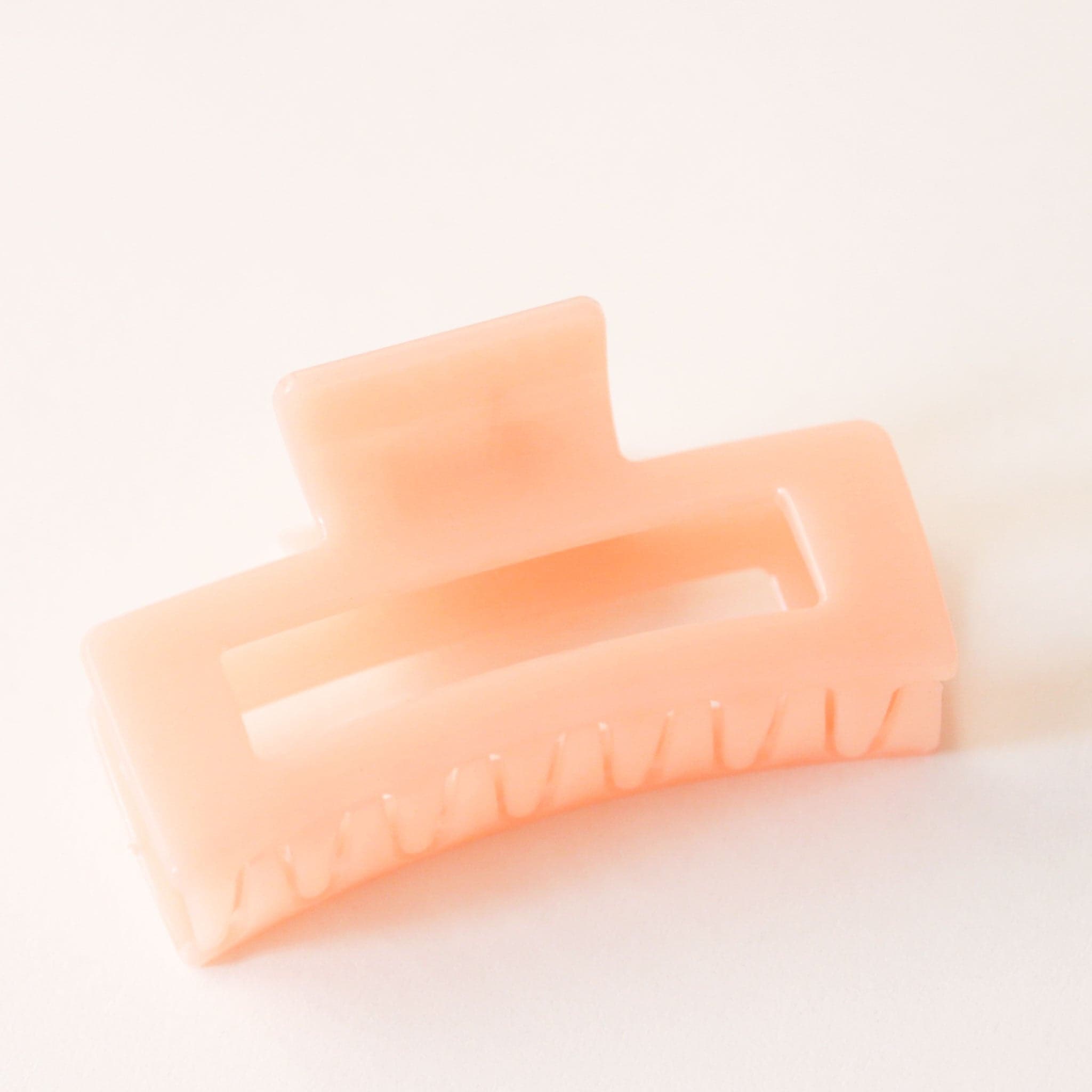 On a white background is a light orange colored rectangular claw clip with a jelly, almost translucent effect.