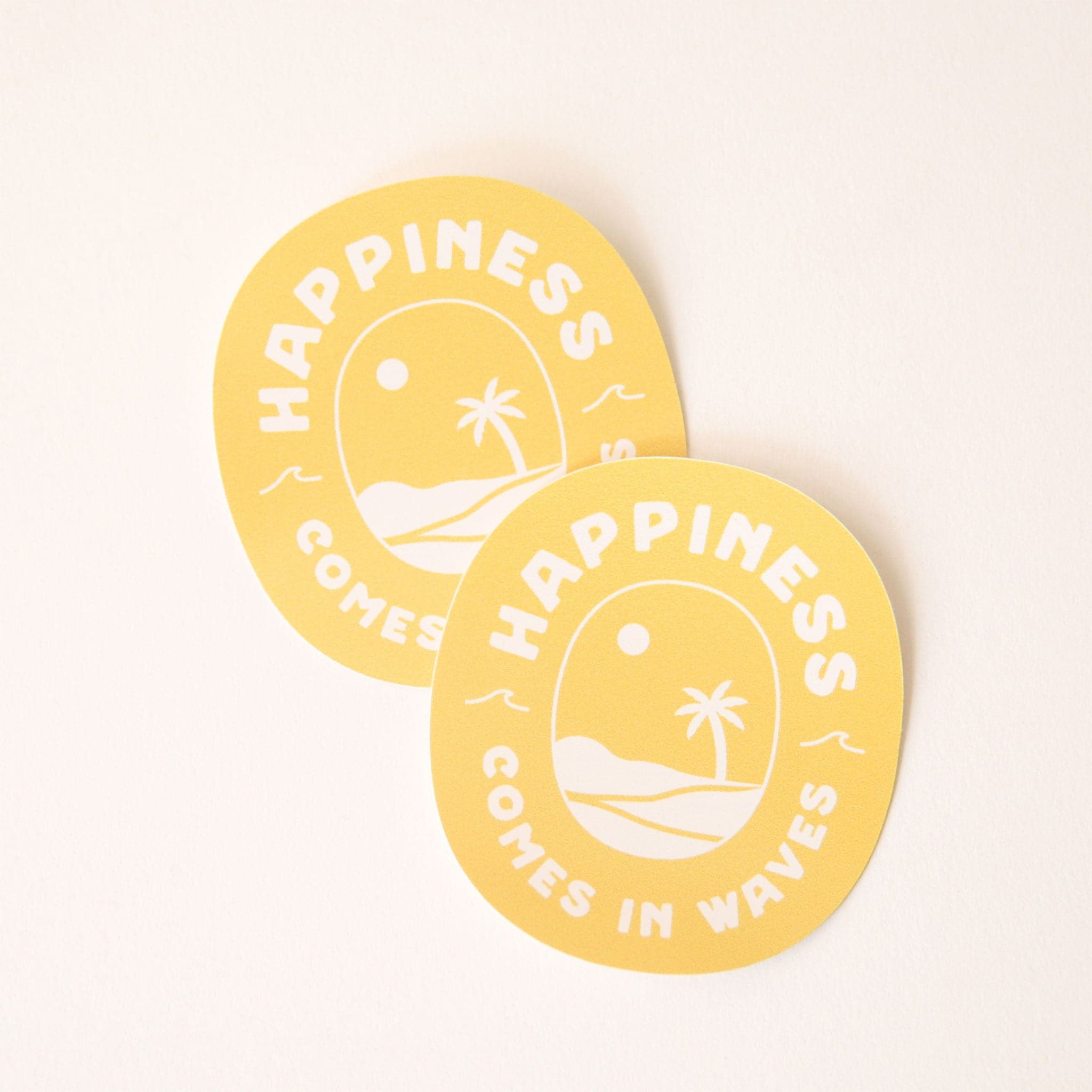A yellow circle vinyl sticker with a beach design featuring a palm tree, a sun and the words "Happiness comes in waves" around the edge of the circle.