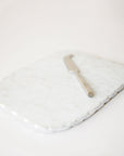 On a white background is a white marble cheese board with a cutting knife and a silver edge.