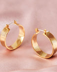 Medium sized gold hoops that have a wider frame and a thin depth. They feature a straight post and a clasp on the back top of the hoop to secure it on your ear.