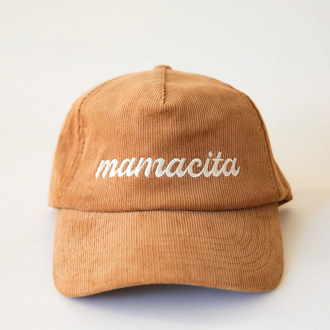 A burnt orange corduroy snapback hat with white cursive text that reads, "mamacita".