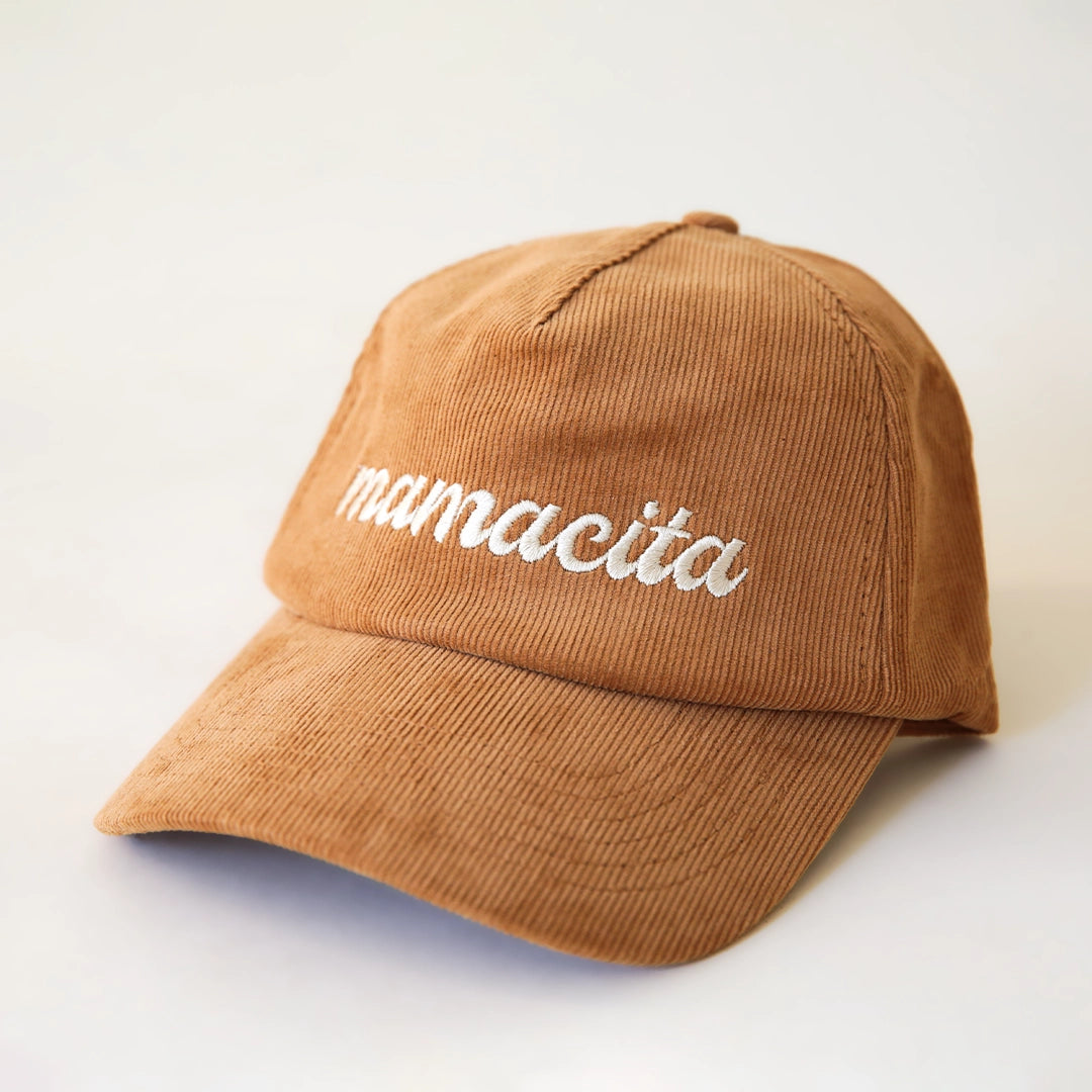 A burnt orange corduroy snapback hat with white cursive text that reads, "mamacita".