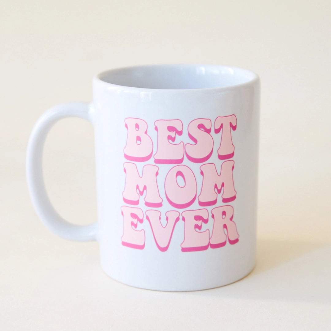 A white ceramic mug with "Best Mom Ever" in pink 70's style bubble writing along with a pink daisy on the back side.