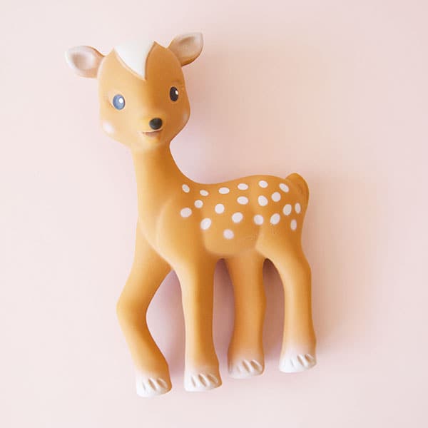 On a light pink background is a fawn children&#39;s toy with cream accents. 
