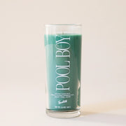 A thin clear glass candle with a green wax candle inside and has white text that reads, "Pool Boy". 