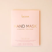 On a cream background is a pink packet with a hand mask inside that reads, "Karuna Hand Mask Hydrating + Treatment".