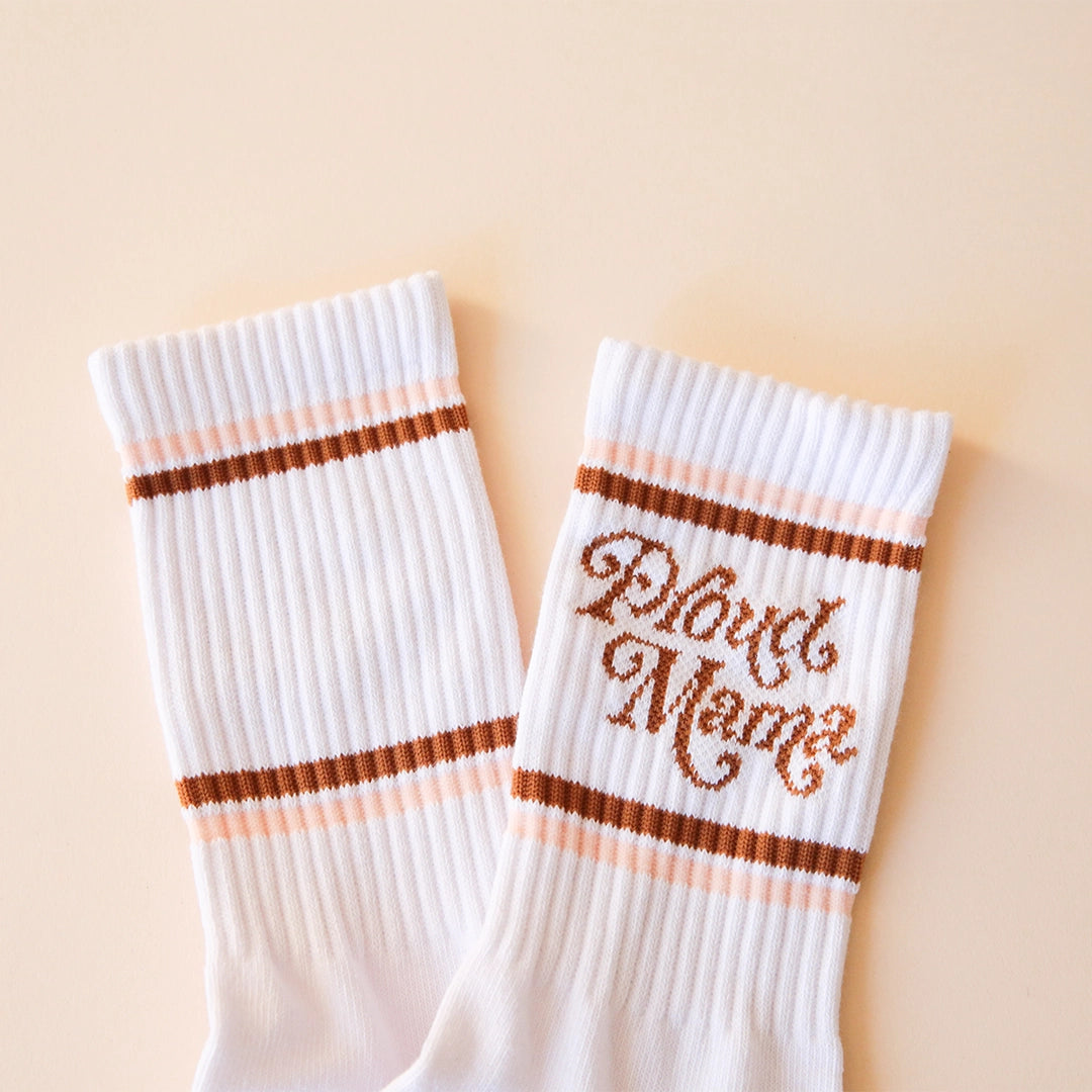 White crew socks with "Proud Mama" written in brown swirly text along with two brown and light pink stripes above and below it.