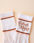 White crew socks with "Proud Mama" written in brown swirly text along with two brown and light pink stripes above and below it.