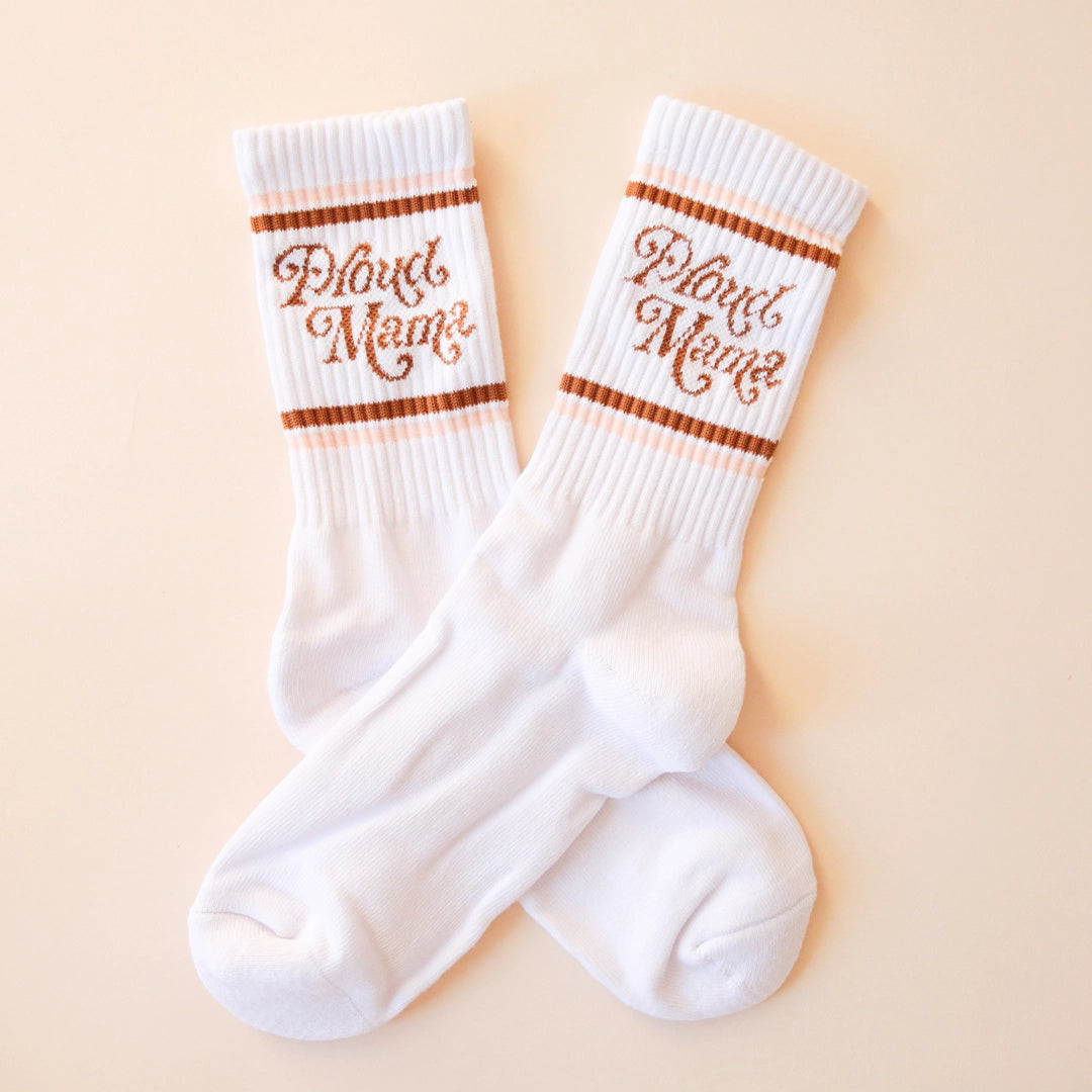 White crew socks with "Proud Mama" written in brown swirly text along with two brown and light pink stripes above and below it.