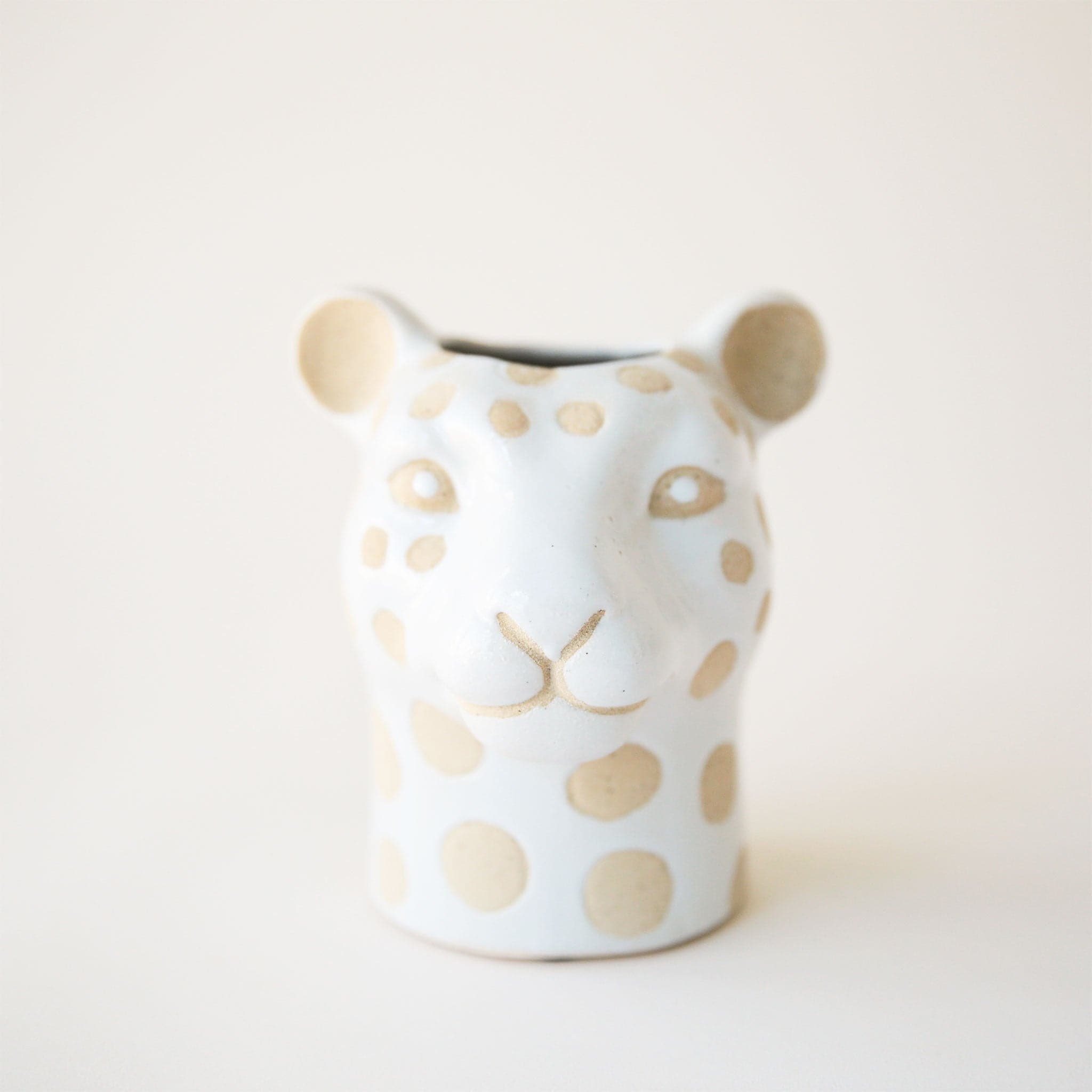 On a cream background is a leopard shaped ceramic planter with tan spots and an opening at the top.