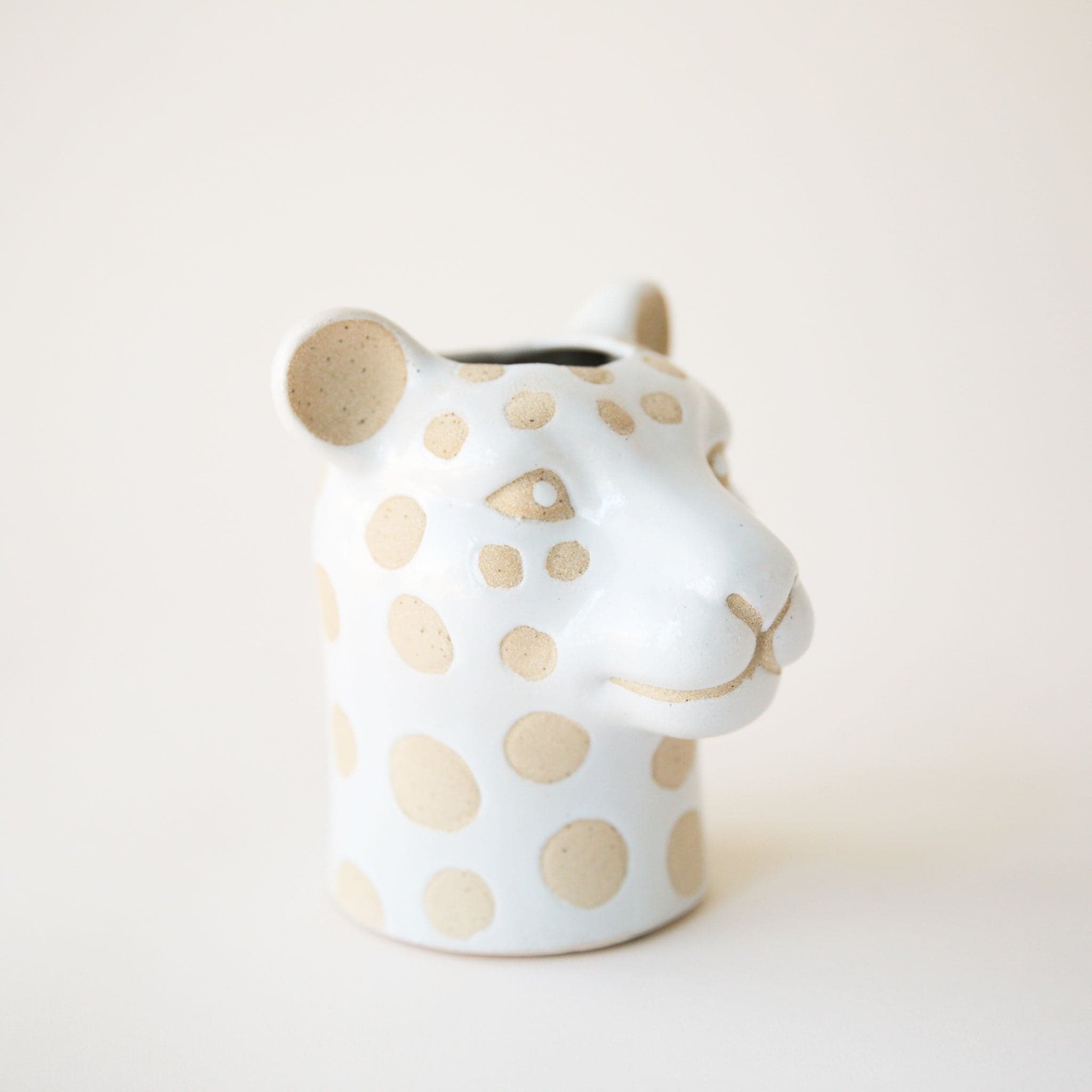 On a cream background is a leopard shaped ceramic planter with tan spots and an opening at the top. 