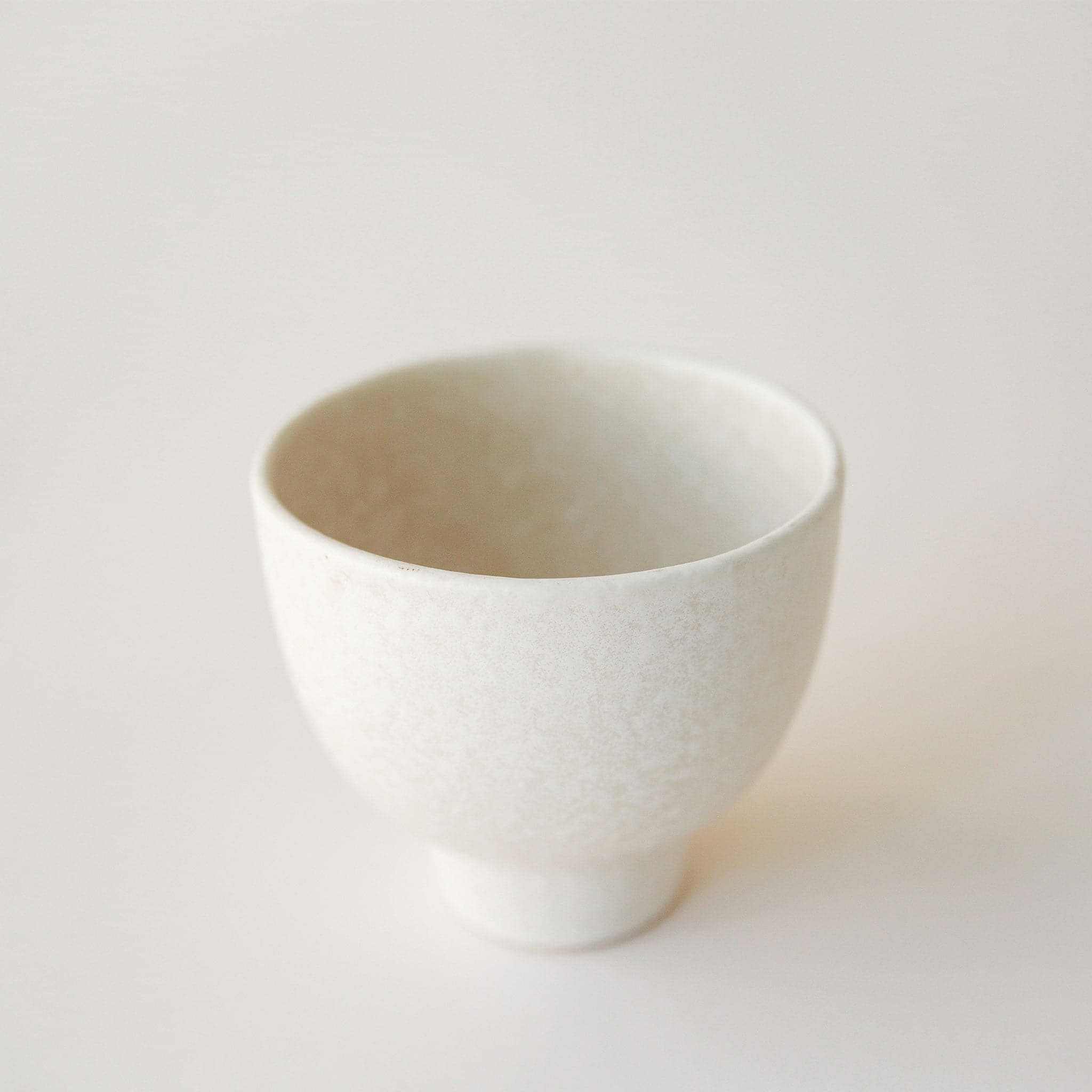 A white pedestal bowl / planter with a slight beige speckling print all over.