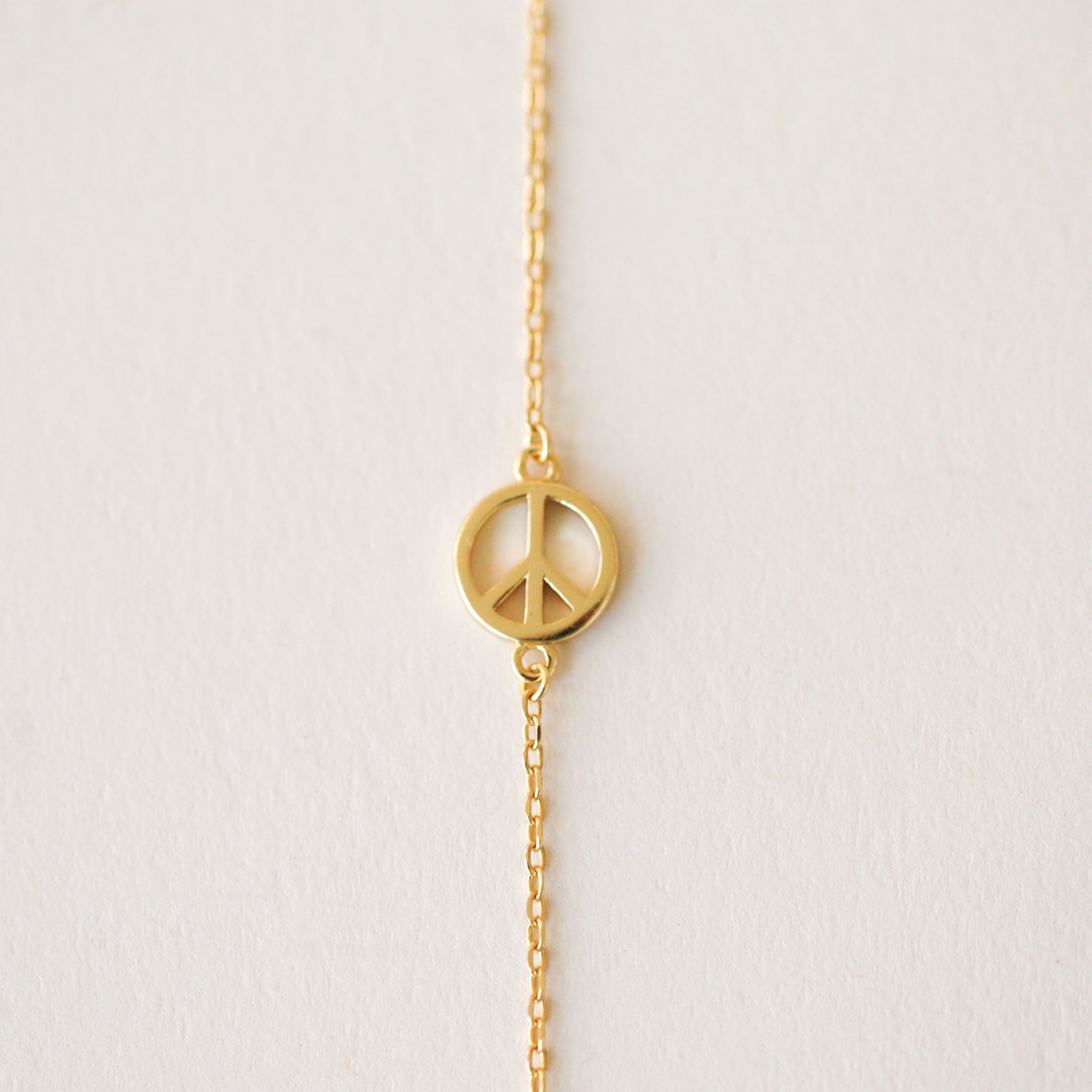 Gold chain necklace complete with classic peace sign symbol pendant. The pendent is connected to the chain by two loops on each side. 