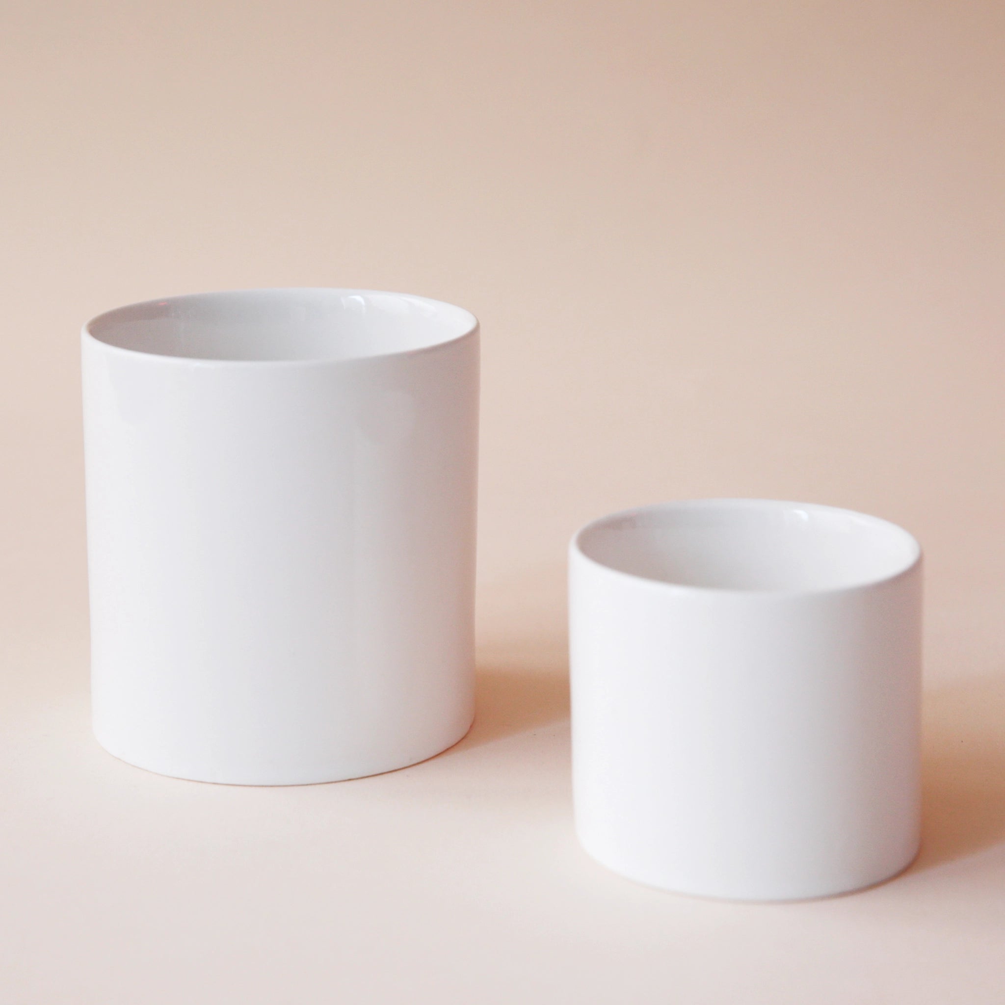 Two different sized cylinder shaped ceramic pots with a glossy finish and a slightly imperfect rim.