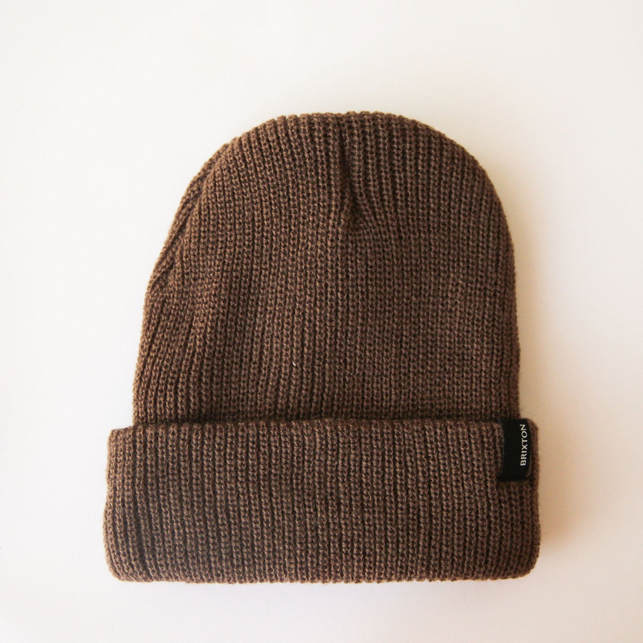 On a cream background is a brown ribbed beanie with a small black Brixton label on the edge of the folded brim. 