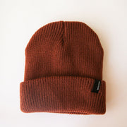 On a cream background is a rust colored ribbed beanie with a small black Brixton label on the edge of the folded brim.